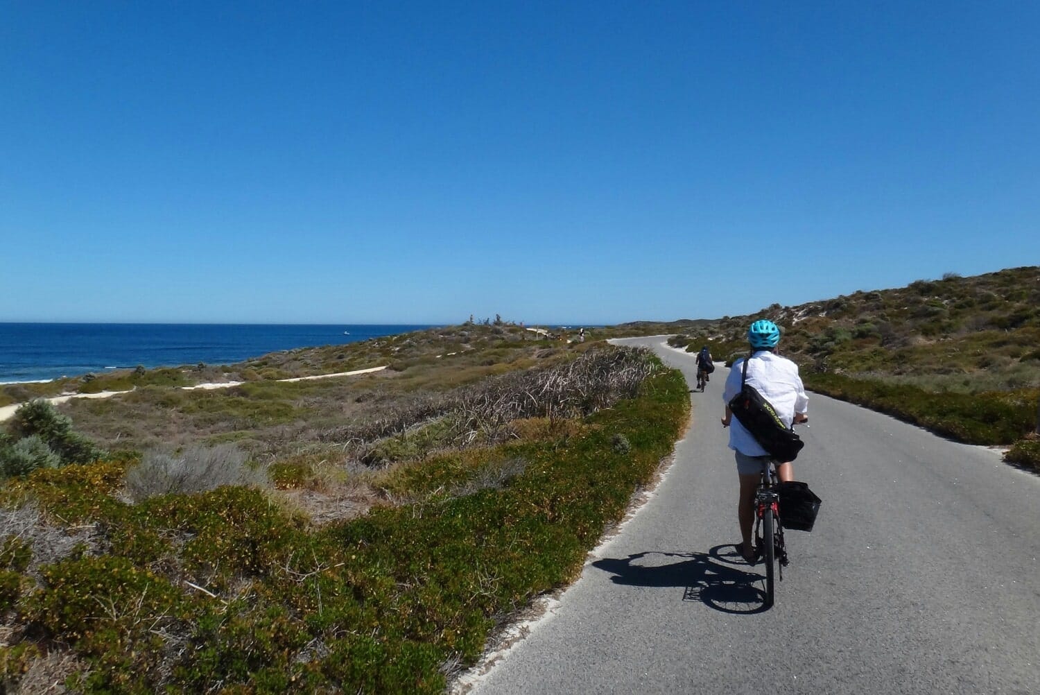 Cyclistes pédalant sur la route asphaltée près de l'océan dans notre article 5 beaux endroits où faire du vélo au Québec #quebec #velo #pistecyclable