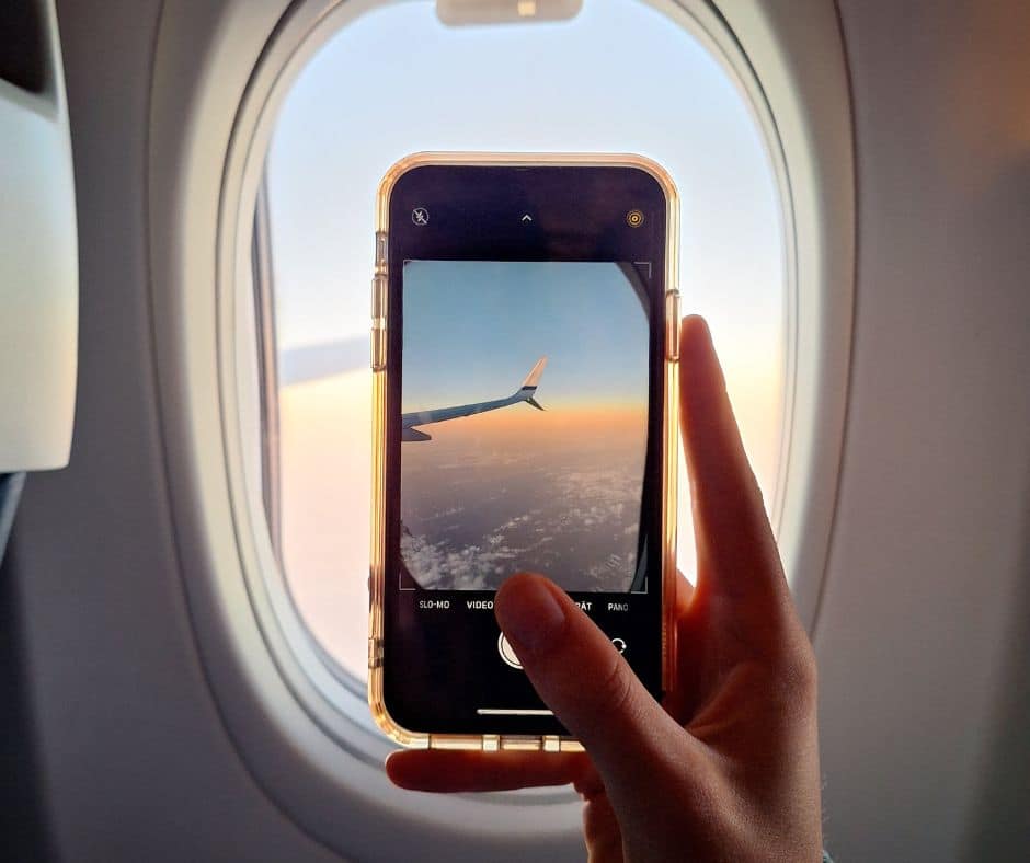 Une personne qui prend une photo de l'aile de l'avion par le hublot grâce à son cellulaire dans notre article Quand la technologie devient l’allier des femmes seules qui explorent le monde #voyagesolo #voyageaufeminin #applicationsmobiles